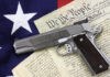 Gun on U.S. Constitution with American flag background.