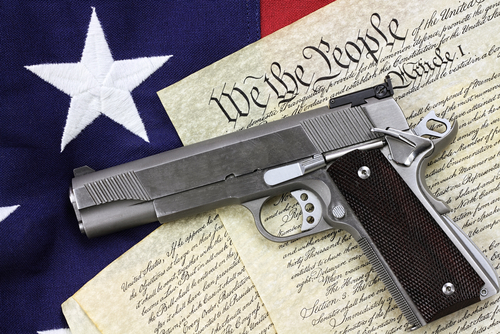 Gun on U.S. Constitution with American flag background.