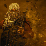 Masked militant holding weapon against fiery background.