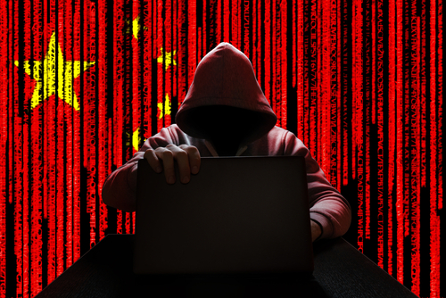 Hooded figure using laptop, China flag background with code.