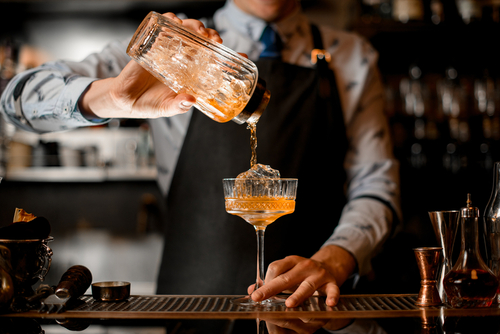 Bartender pouring a cocktail into a glass.