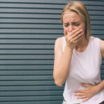 Woman covering mouth with hand and holding stomach.