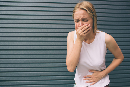 Woman covering mouth with hand and holding stomach.