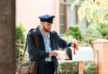 Mail carrier placing envelope in a residential mailbox.