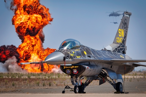F-16 fighter jet on the ground with an explosion in the background