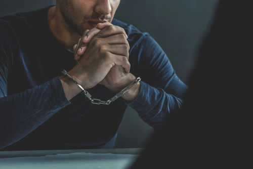 shutterstock_1102701539 Man in handcuffs sitting at a table.