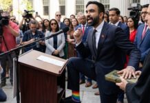 MAMDANI SNUBS Iconic Parade: First Time Since ’64….. A speaker at a podium passionately addressing a crowd, wearing rainbow socks