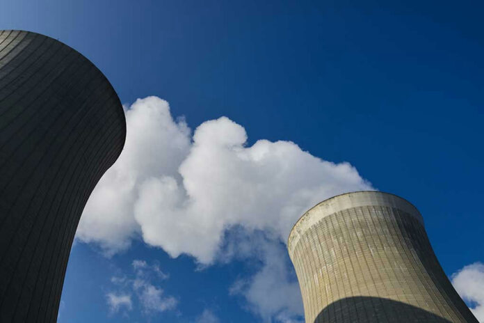 1937096560 Cooling towers emitting steam under a clear blue sky.