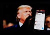Hand holding smartphone displaying Twitter profile.