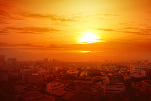 Heatwave,On,The,City,With,The,Glowing,Sun,Background.,Heatwave A vibrant sunset over a city skyline with buildings silhouetted against the orange sky