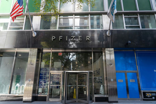 shutterstock_1836084403 Pfizer headquarters building entrance with glass doors and flags.