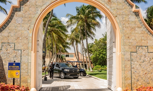shutterstock_2476204587 View through an ornate archway leading to a tropical entrance with palm trees and parked cars