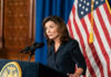 NY Governor is Now Begging to the Rich – See Why Woman speaking at podium with American flag backdrop.