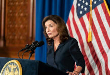 NY Governor is Now Begging to the Rich – See Why Woman speaking at podium with American flag backdrop.