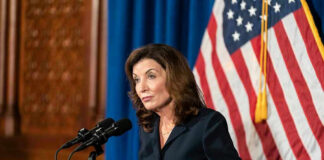 Woman speaking at podium with American flag backdrop.