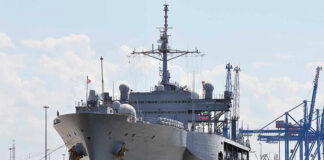 Large naval ship docked at an industrial port.
