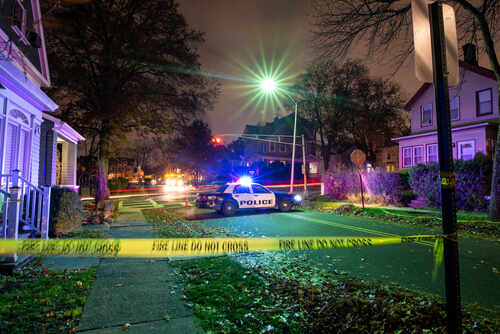 Police car with flashing lights at a crime scene surrounded by caution tape