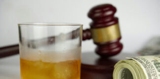 A glass of whiskey next to a gavel and rolled money