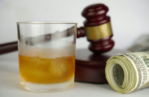 shutterstock_1998599522 A glass of whiskey next to a gavel and rolled money