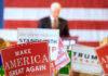political rally with speaker and campaign signs in front of an American flag